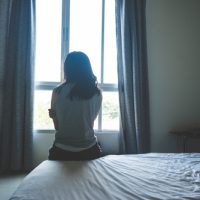 Woman,Sitting,On,Bed,In,Room,With,Light,From,Window